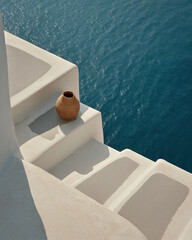 Obraz premium A rustic clay vase rests on whitewashed Santorini steps overlooking the shimmering turquoise Aegean Sea.