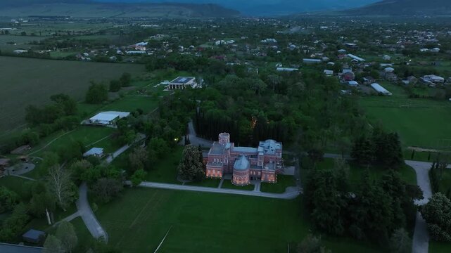 Aerial view of Chateau Mukhrani royal palace and estate in Georgia, magnificent pink castle architecture with a tower surrounded by a lush green park, gardens and pathways on a spring day.