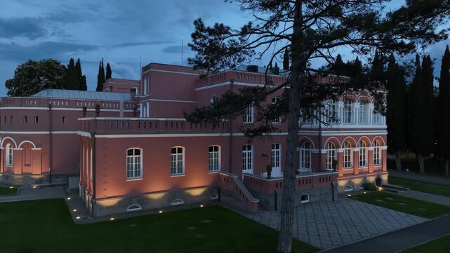 Aerial view of Chateau Mukhrani royal palace and estate in Georgia, magnificent pink castle architecture with a tower surrounded by a lush green park, gardens and pathways on a spring day.