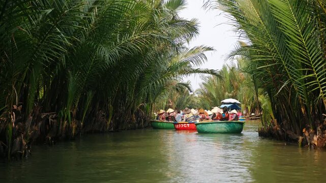 Tourists sailing on basket boats through a lush coconut palm forest river in hoi an, vietnam