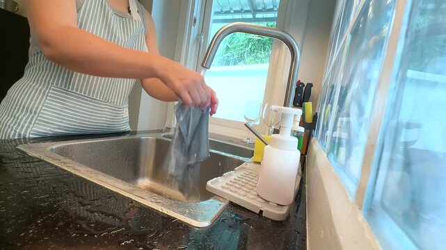 Woman rinsing and wringing a kitchen cloth in sink. Real life video footage of household cleaning, washing dishcloth, kitchen hygiene and everyday home routine.