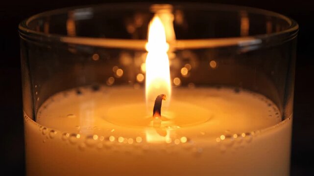 A close-up view of a burning candle in a glass jar, showcasing the flickering flame and melted wax, creating a warm ambiance