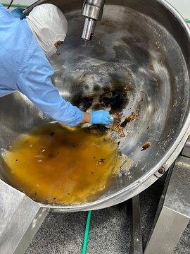 Worker cleaning an industrial mixing kettle after food production. Sanitation procedure performed to remove product residues and prepare equipment for the next manufacturing batch while maintaining fo