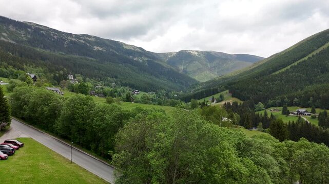 Aerial view of a mountain valley with scattered chalets forested slopes and a winding road in Krkono&scaron;e Czech Republic