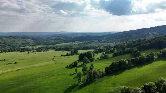 Aerial view of green hills with meadows trees and forested ridges under a dramatic sky in summer