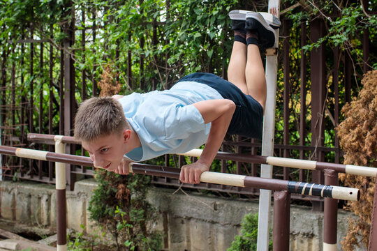 Teenage boy practicing street workout exercise on parallel bars in backyard fitness area, adolescent athlete maintaining challenging static position, showcasing flexibility, coordination and upper bod