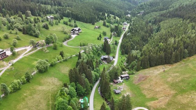 Aerial view of mountain village in green forested valley with houses and meadows in summer
