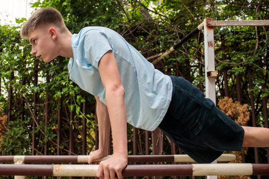 Teenage boy practicing street workout on outdoor parallel bars, focused adolescent athlete maintaining strong support position while developing coordination, endurance and functional fitness skills