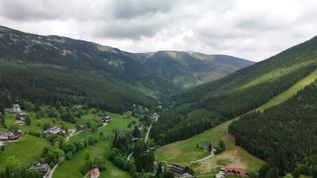Drone flight over green mountain valley with forest and scattered cottages in the Krkono&scaron;e Mountains Czech Republic 
