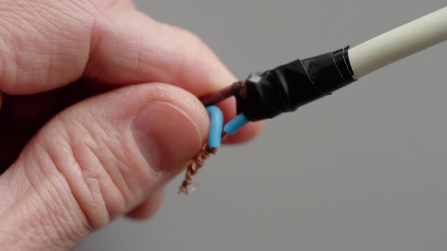 Closeup hands wrapping tape over blue and brown conductors and white sheath, careful insulation of colorcoded wires, neat layering and secure electrical finish