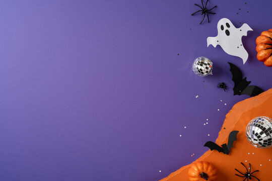 Happy Halloween flatlay with pumpkin, ghost, bats and disco balls on purple and orange background