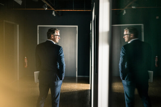 Mature businessman standing on office floor holding laptop