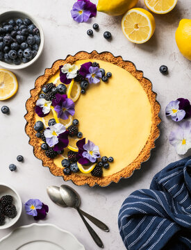 Overhead view of a lemon tart with berries and flowers.