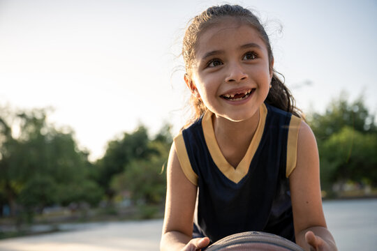Joyful young girl playing basketball outdoors