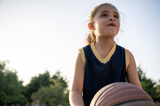 Hopeful young girl holding a basketball outdoors