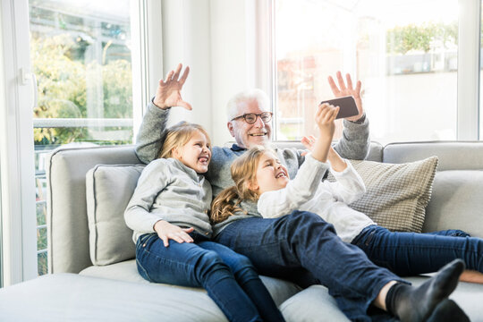 Two happy girls and grandfather on sofa taking a selfie