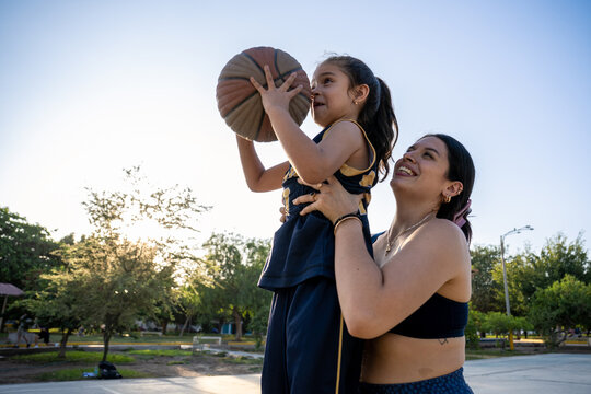 Mother helping young daughter shoot a basketball