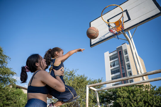 Mother helps her daughter shoot a basketball
