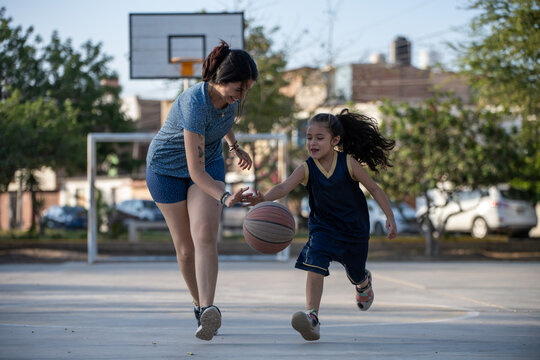 Mother teaching young daughter to play basketball outdoors