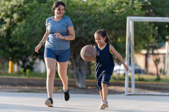 Happy mother and daughter playing basketball outdoors