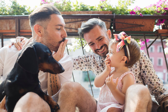 Happy gay couple with daughter and dog on balcony