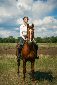 Woman riding a brown horse in a grassy field