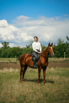 Woman riding a brown horse in a grassy field