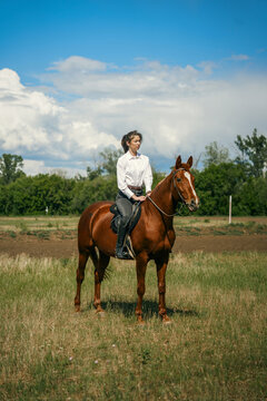 Woman riding a brown horse in a grassy field