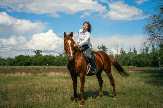Woman riding a brown horse in a grassy field