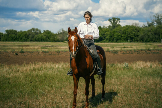 Woman riding a brown horse in a grassy field