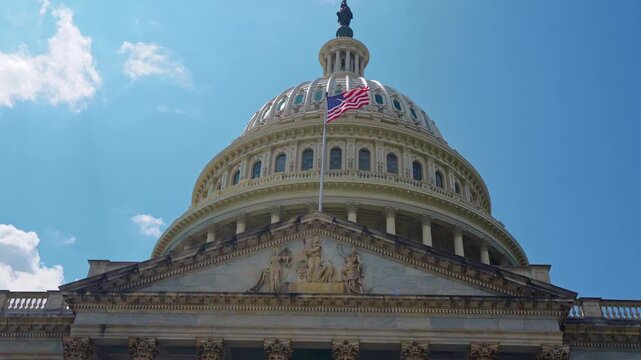 American flag waving on Capitol architecture. American flag in sky. American flag for freedom symbol. American flag on historic dome.