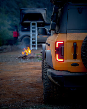 Overlanding vehicles parked at a forest campsite with a fire