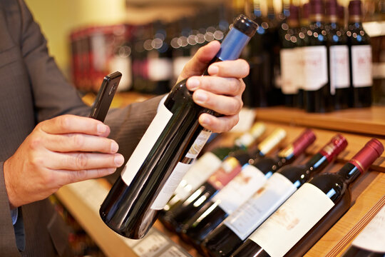 Germany, Cologne, Mature man taking picture of wine bottle in supermarket