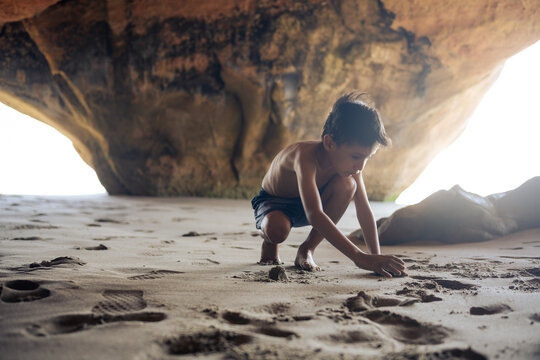 Young boy exploring sand inside a scenic beach cave
