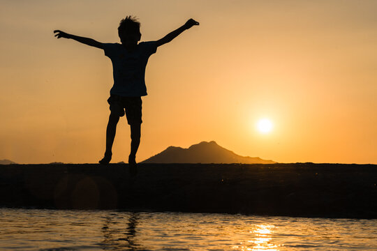 Silhouette of a young boy jumping outdoors at sunset