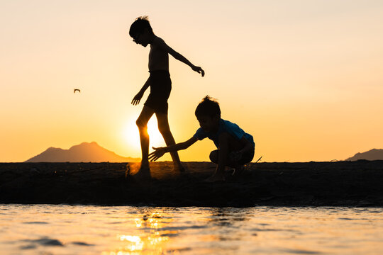 Silhouetted young boys playing near water at sunset