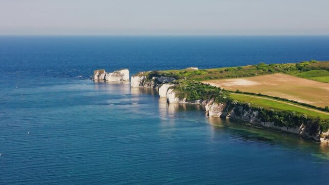 Aerial drone footage of Old Harry Rocks and the surrounding Dorset coastline in England, showing white chalk cliffs, sea stacks, calm blue sea, farmland, and green clifftop fields.
