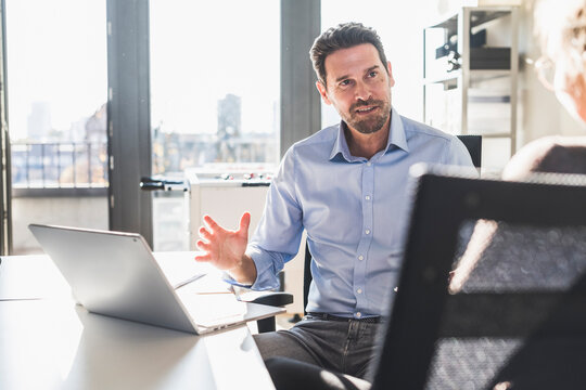 Businessman using laptop while discussing with colleague at office