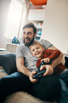 Laughing father and little son sitting together on the couch playing computer game