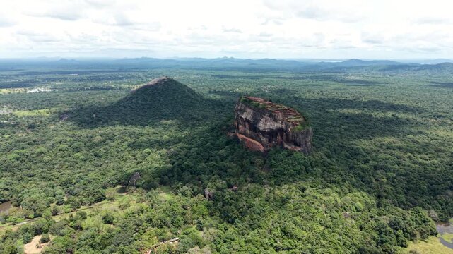 Aerial view of the ancient Sigiriya Lion Rock fortress and Pidurangala Rock rising above the dense tropical jungle under a cloudy sky in Sigiriya, Central Province, Sri Lanka.