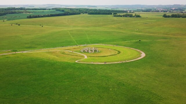 Very wide aerial drone footage of Stonehenge in Wiltshire, England, showing the ancient prehistoric stone circle set within the open green grassland of Salisbury Plain.