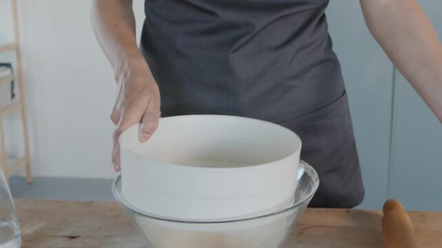 Woman baker sifting flour for dough preparation