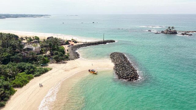 Aerial view of the tropical coastline with stone breakwaters and turquoise water in Peraliya, Southern Province, Sri Lanka.