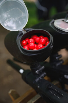 Close-up of paintball marker hopper filled with red paintballs before outdoor game. Recreational shooting equipment prepared for team competition and tactical sport activities.