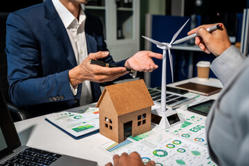 Business team discussing renewable energy and green housing at office desk with wind turbine model,...