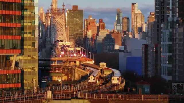 Evening sun illuminates a long island city subway train as it arrives at a station with the ed koch queensboro bridge and manhattan skyline in the distance.