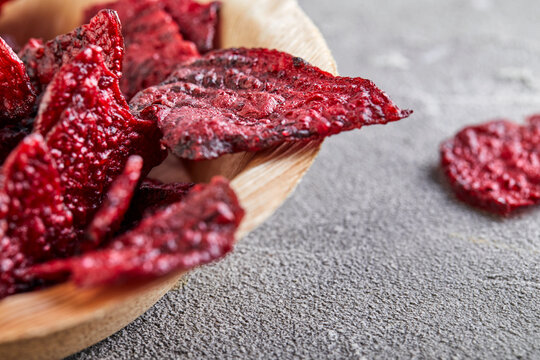 Diet healthy eating concept. Dried beet chips or baked beets in a wooden bowl, on a gray concrete background. Organic natural food. Copy space.