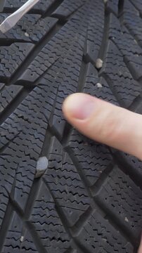 Mechanic hand removes gravel stuck inside rubber tread. Each stone can weaken grip. Autumn preparation ensures that winter tire delivers full stability