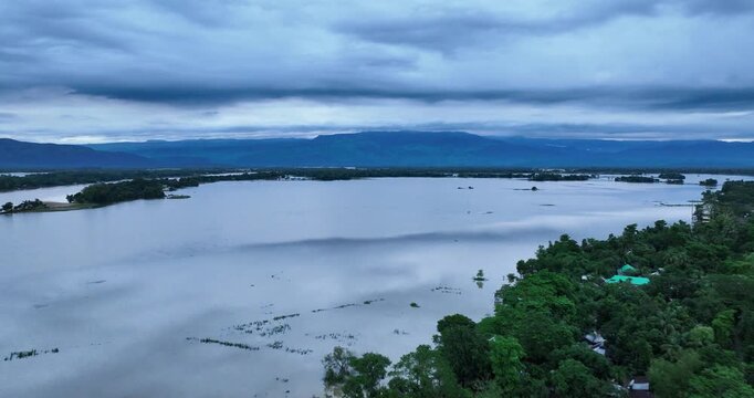 Aerial view of Tanguar Haor wetland surrounded by lush green trees and distant hills under a cloudy sky in Sunamganj District, Sylhet Division, Bangladesh.