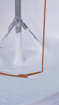 Mixer tool enters white paint in bucket, rotating to achieve smooth consistency. Prepare paint for application on walls or surfaces during home renovation or new building construction
